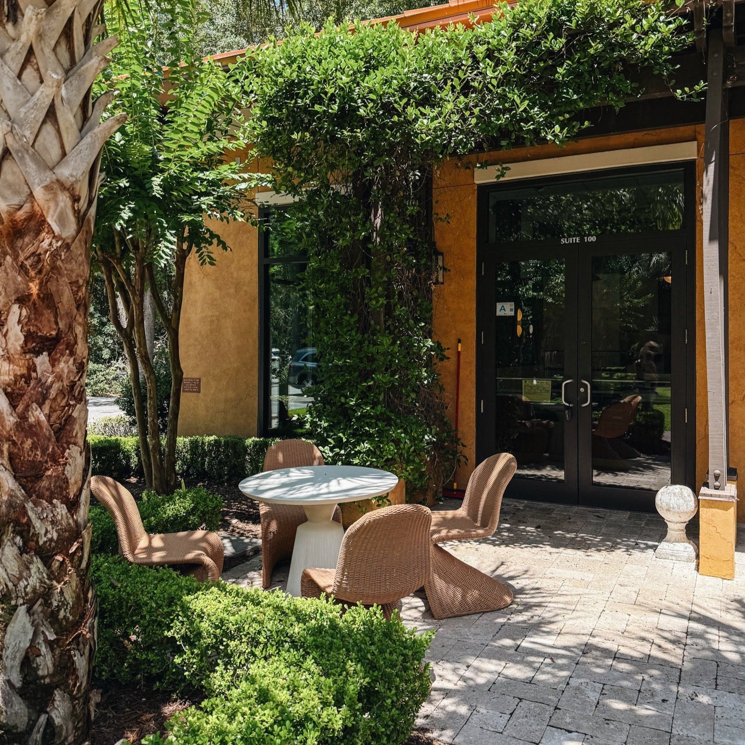 Outdoor seating area with tables and chairs in front of a building entrance. | Origin Coffee Bar | Savannah, Georgia and Hilton Head Island, South Carolina | Specialty Coffee Roaster and Cafe