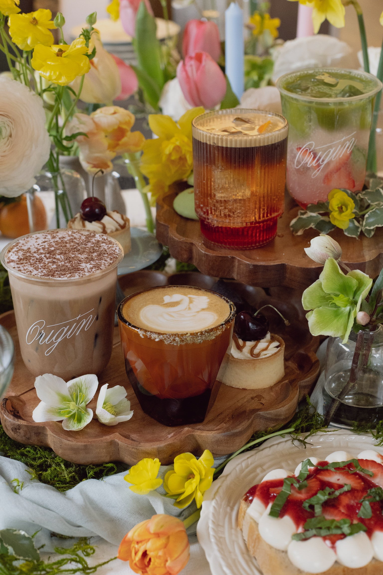Assorted beverages and desserts on a wooden tray with flowers in the background